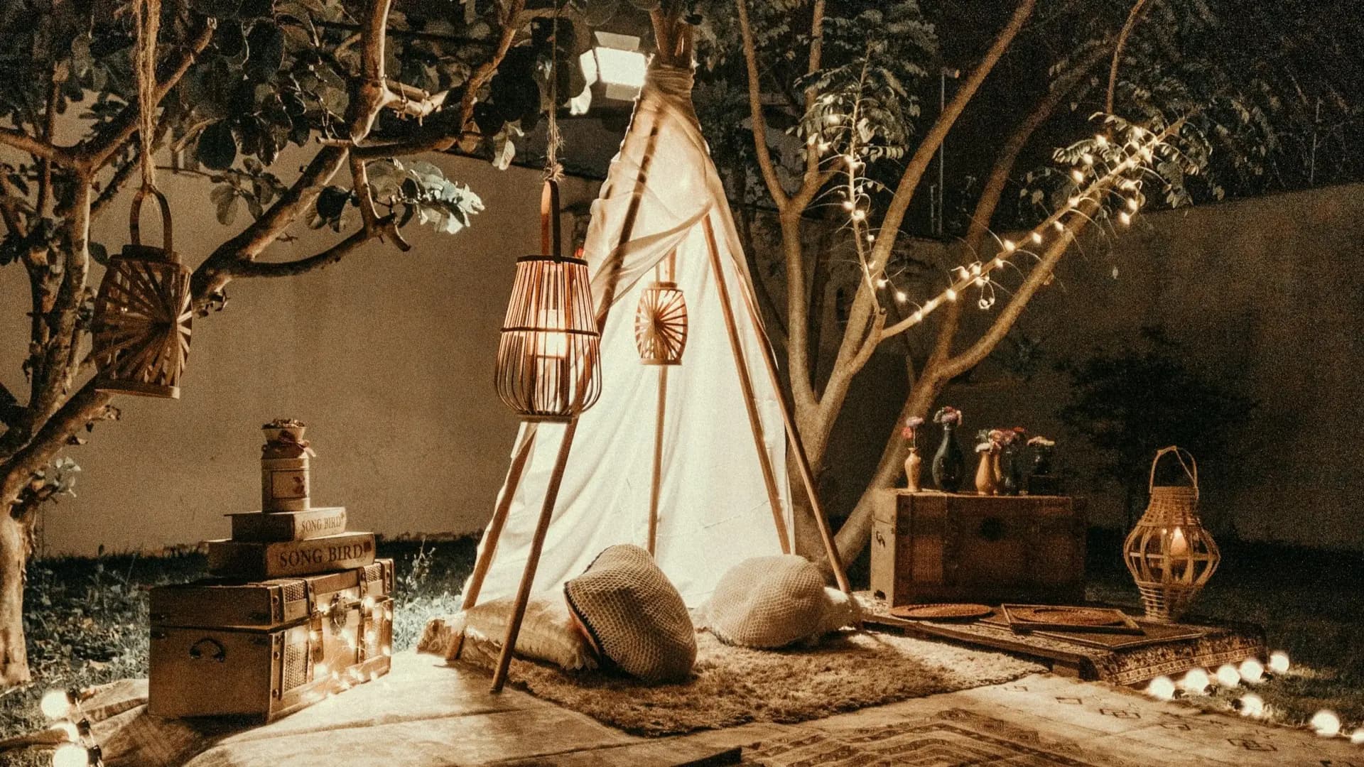 Gemütliches Zelt im Garten bei Nacht mit warmen Lichterketten, Laternen, Kissen und einem Teppich.